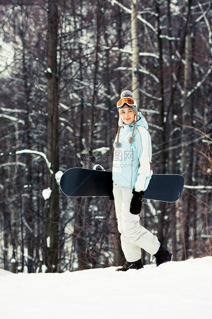 年轻美女拿着雪板在滑雪坡上行走图片
