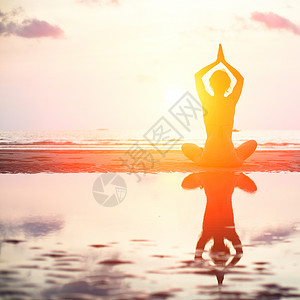 日落时坐在沙滩上露莲花的瑜伽妇女在水中图片