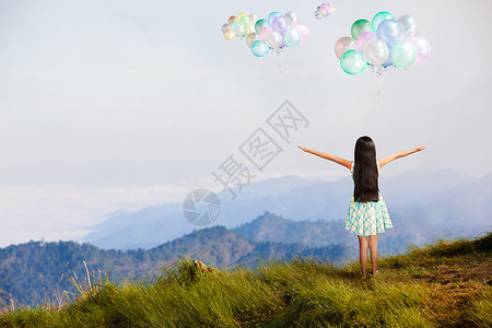 女孩站在高山上仰望天空的气球自由的概念图片