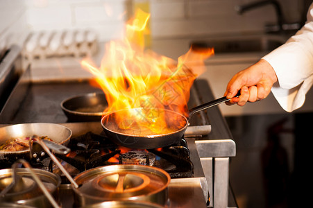 厨师在厨房炉灶上的煎锅中用火焰烹饪图片