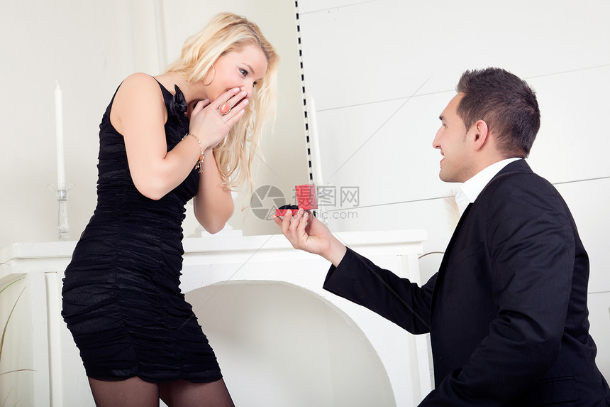 英俊的年轻帅男跪在膝盖上向一位美丽的金发美女求婚她满怀惊喜图片