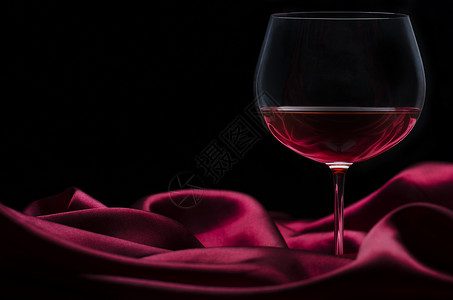 深色背景的红丝绸上的一杯酒图片