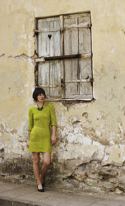 身着绿或黄衣服的妇女靠在爱沙尼亚塔林老城的一堵有心脏形状或洞的百叶窗图片