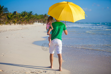 年轻父亲和女儿的背影躲在黄色雨伞下躲避太阳图片