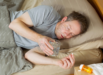 成年男子躺在床上时准备用水取药的横向照片图片