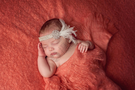 一个十周大的小女孩穿着闪光灯和羽毛头带她睡在桃色的毯子背景图片