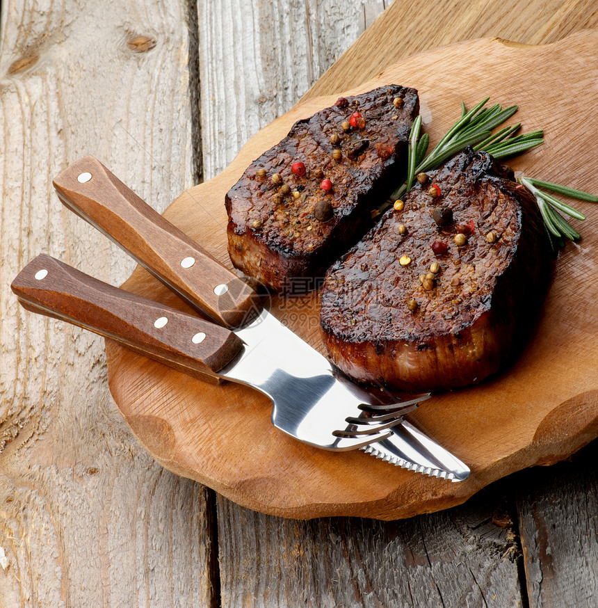 烤牛排配香料和迷迭香在木板上用叉子和餐桌刀在质图片