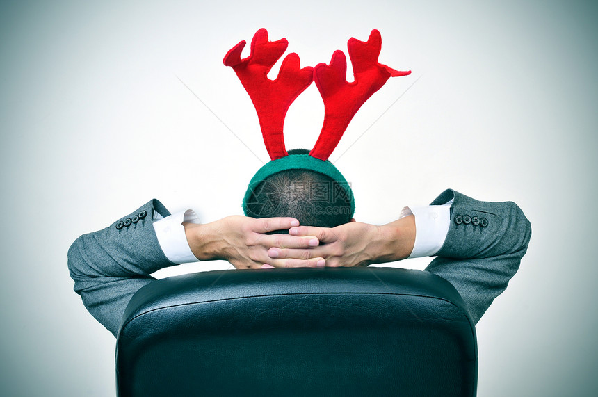 一个男人带着驯鹿角头带在办公室圣诞晚会后坐在图片