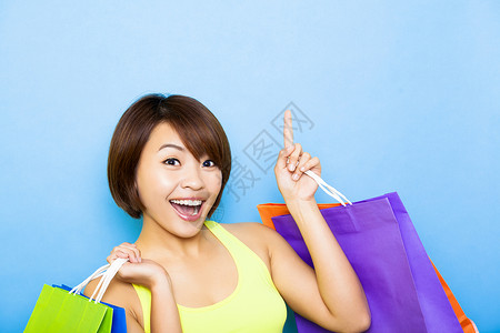 年轻女子提着购物袋向上指着背景图片
