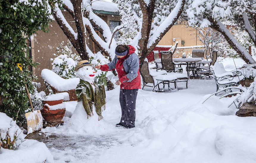 一个女人在暴风雪期间在她的前院堆雪人图片