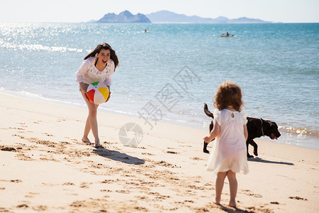 快乐的年轻母亲在海滩上与女儿和狗玩得开图片