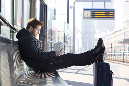 在火车站平台上用袋子和移动电话轻松放的男图片