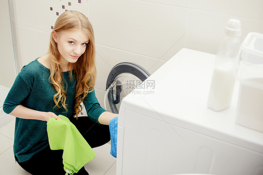 金发女人把脏衣服放在洗衣机里洗衣机上有洗衣粉图片