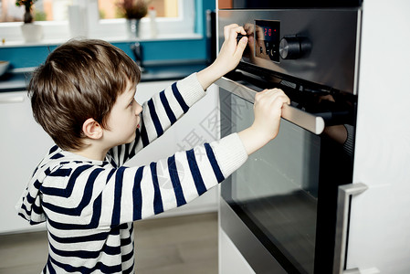 好奇的小男孩在和烤箱的把手玩耍时很危险图片