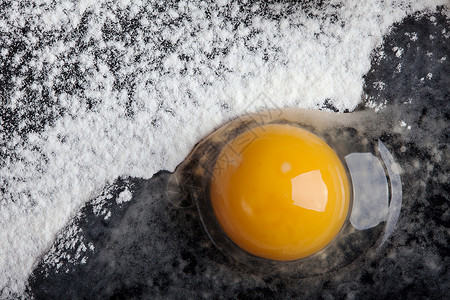 黑色背景上一层面粉上的破鸡蛋背景图片