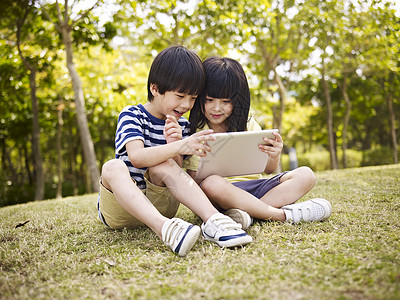 小亚洲女孩和男孩坐在草地上图片