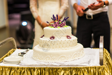 银色底座和紫罗兰糖花上的多层白色婚礼蛋糕图片