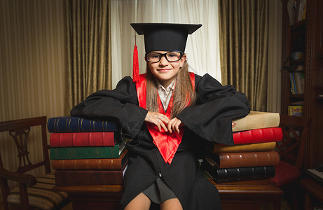 穿着毕业服装的小天才女孩的肖像在图书图片