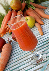 一杯新鲜的苹果胡萝卜汁在木质表面上背景中的新鲜胡萝卜图片