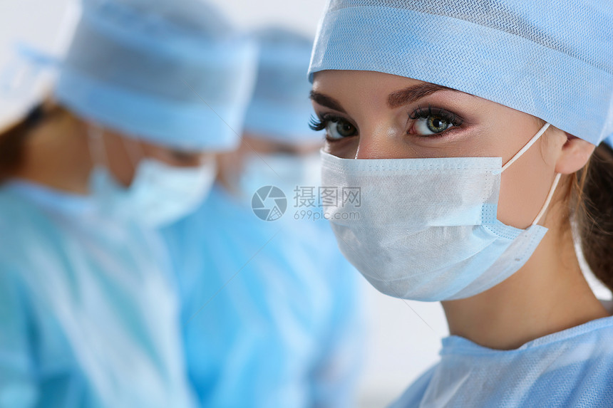 三名外科医生在手术室工作复苏医学团队戴着防护口罩拯救病人手术和紧急情况的概念看着相机的女图片