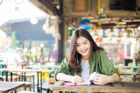 亚洲女人坐在木桌上在户外微笑着看书图片