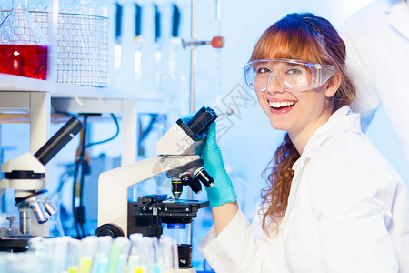 年轻有吸引力的女研究科学家在看生命科学实验室的显微镜幻灯片时玩得开心图片