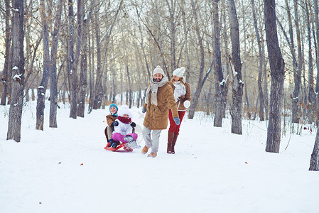 快乐的男子骑着小孩在雪橇上同时在冬季图片