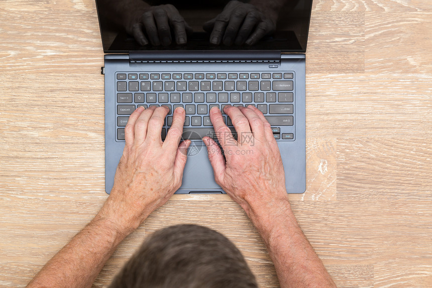 高级天主教成年男子在木制桌上的笔记本电脑键盘上打字图片