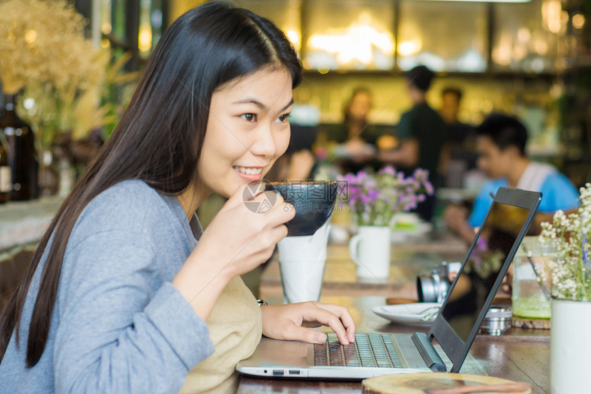 亚洲女在咖啡店用笔记本电脑与图片