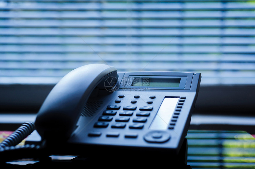 带有传统有线耳机的行政VoIP桌面电话和背景中的商务办公室百叶窗浅景深专图片