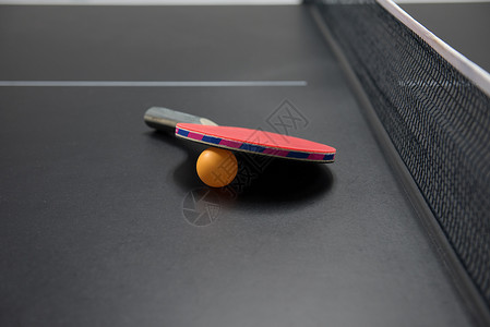 黑桌上有橙色球的乒乓球拍图片