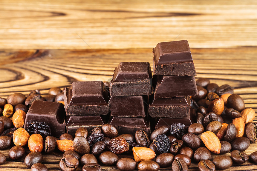 黑巧克力立方咖啡豆花生和木制桌上的葡萄干闭合图片