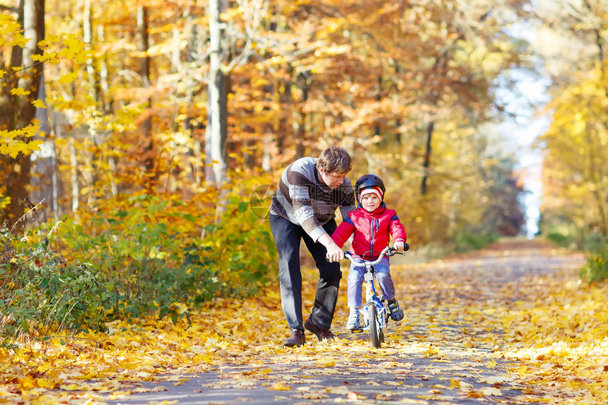 岁的小男孩和他的父亲在秋天的森林里骑着自行车爸教儿子积极的家庭休闲带头盔的孩子运动休闲图片