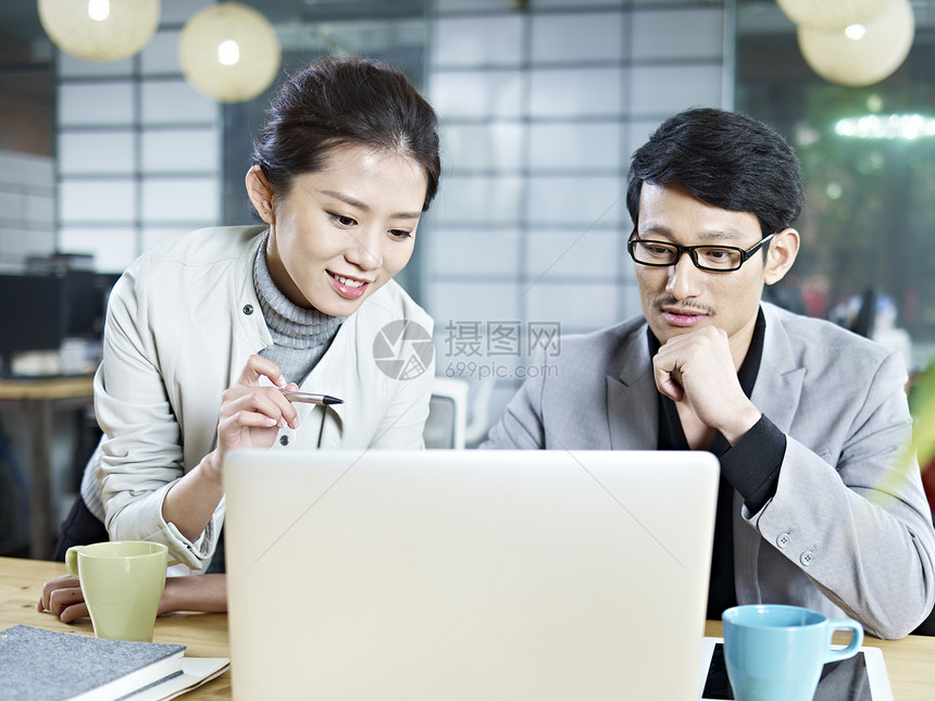 两位年轻的亚洲人公司人士使用笔记本电脑讨论办公事图片
