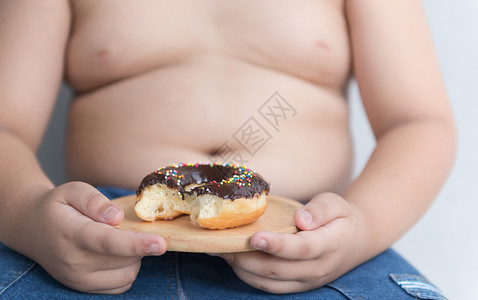 木盘上的甜圈手握灰色背景的肥胖男孩图片
