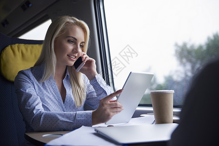 商业女商人通过手机和火车上使用数字平板电脑图片