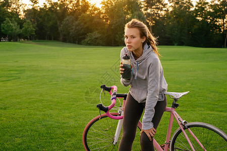 运动妇女在公园骑自行车后在公园里喝水图片