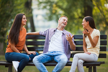 三个朋友坐在公园的长椅上聊天图片