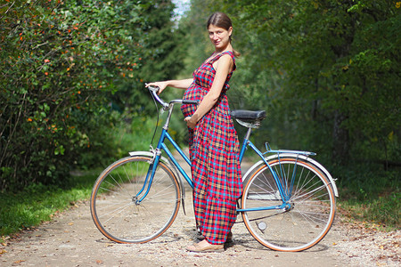 身着红色格子裙和自行车在森林路边一旁的林道上骑脚踏图片