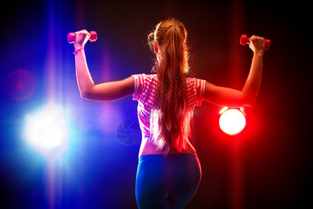 身材瘦弱的体育健身女孩在健身房的多色光线下工作图片