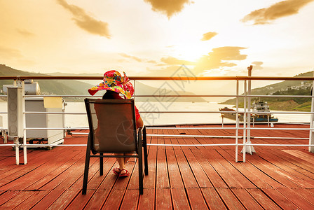 戴着大帽子的女人在游轮的甲板上看日出背景图片