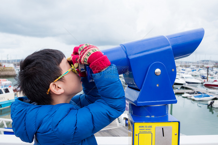 用望远镜看港口的亚洲小男孩图片