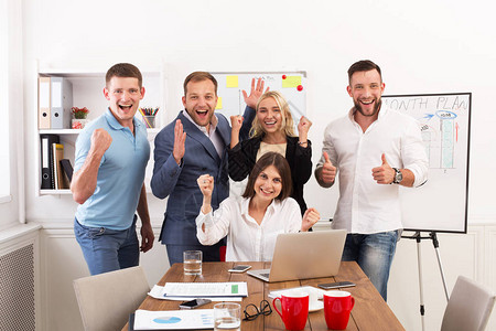 我们赢了快乐的商界人士在办公室的笔记本电脑屏幕附近庆祝成功成功的合作伙伴和同事背景图片