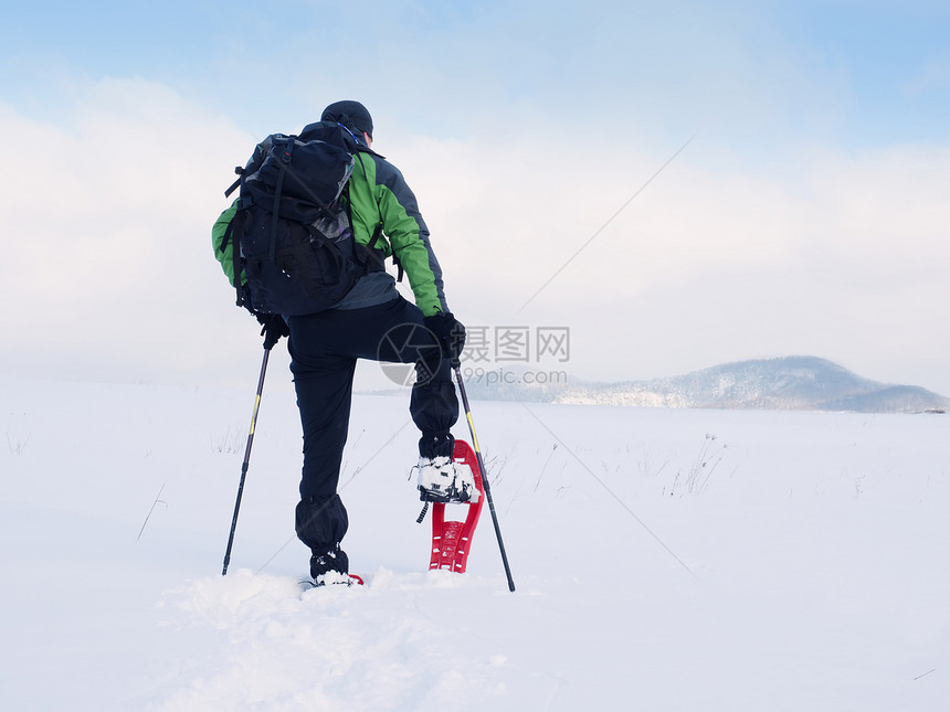 清洁雪鞋的人穿着绿色灰冬季夹克和黑色徒步裤的徒步旅行者在雪域中行走粉雪中的雪鞋行走多云的冬日图片