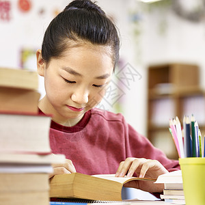 在教室里读一本厚书的亚洲小学生图片