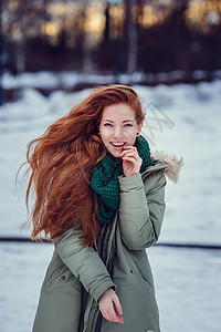 穿着大衣和绿围巾的快乐红头发女孩在冬季雪图片