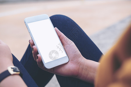 一名坐在街上用空白屏幕拿着手机的妇女的假相照片Moc图片