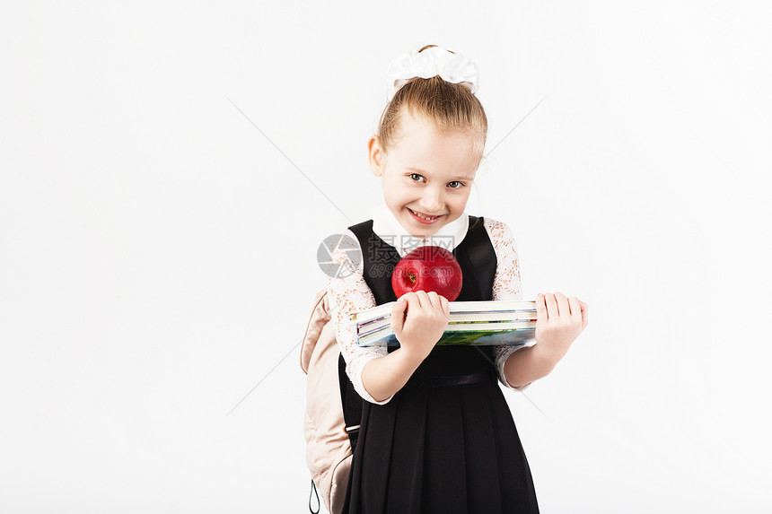 孩子微笑的小女孩背着大背包拿着书和白色背景的大红苹果看着相机学校理图片
