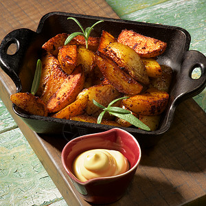黑卡斯特伊龙锅里有美味的烤土铃薯炉和木制板上含奶酪酱的热煎饼图片