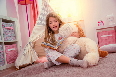 可爱的小女孩在她的房间里看书图片